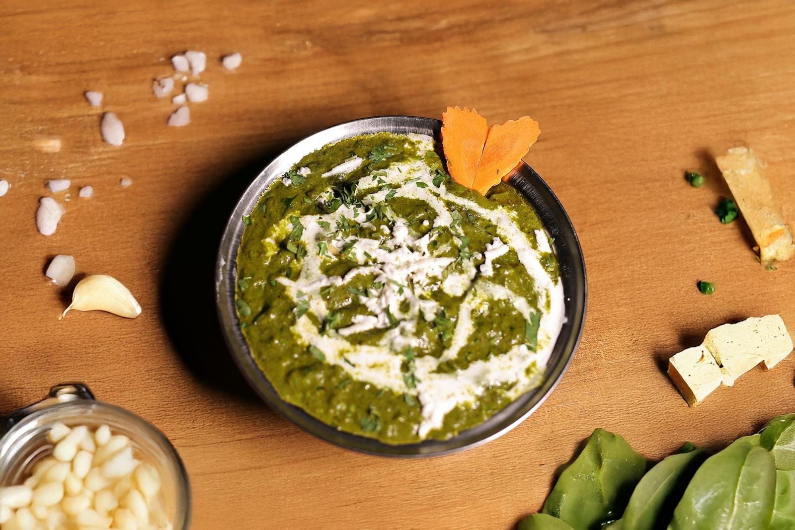 Top view of traditional Indian Palak Paneer garnished with cream and vegetables.